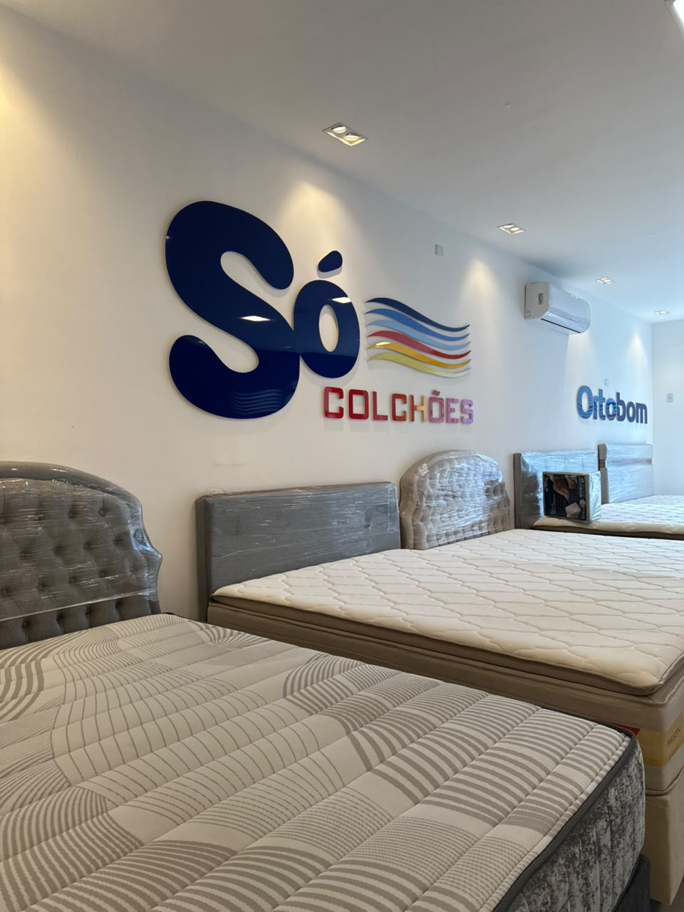 Logo Só Colchões na parede da loja com camas expostas