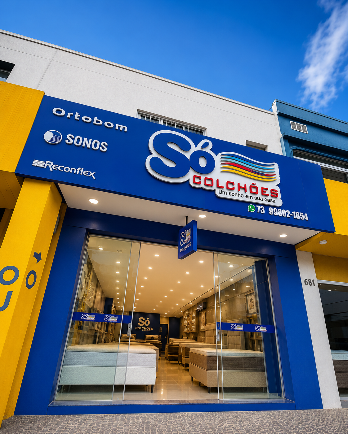 Fachada da loja Só Colchões em azul e amarelo, com painéis das marcas Ortobom, Sonos e Reconflex